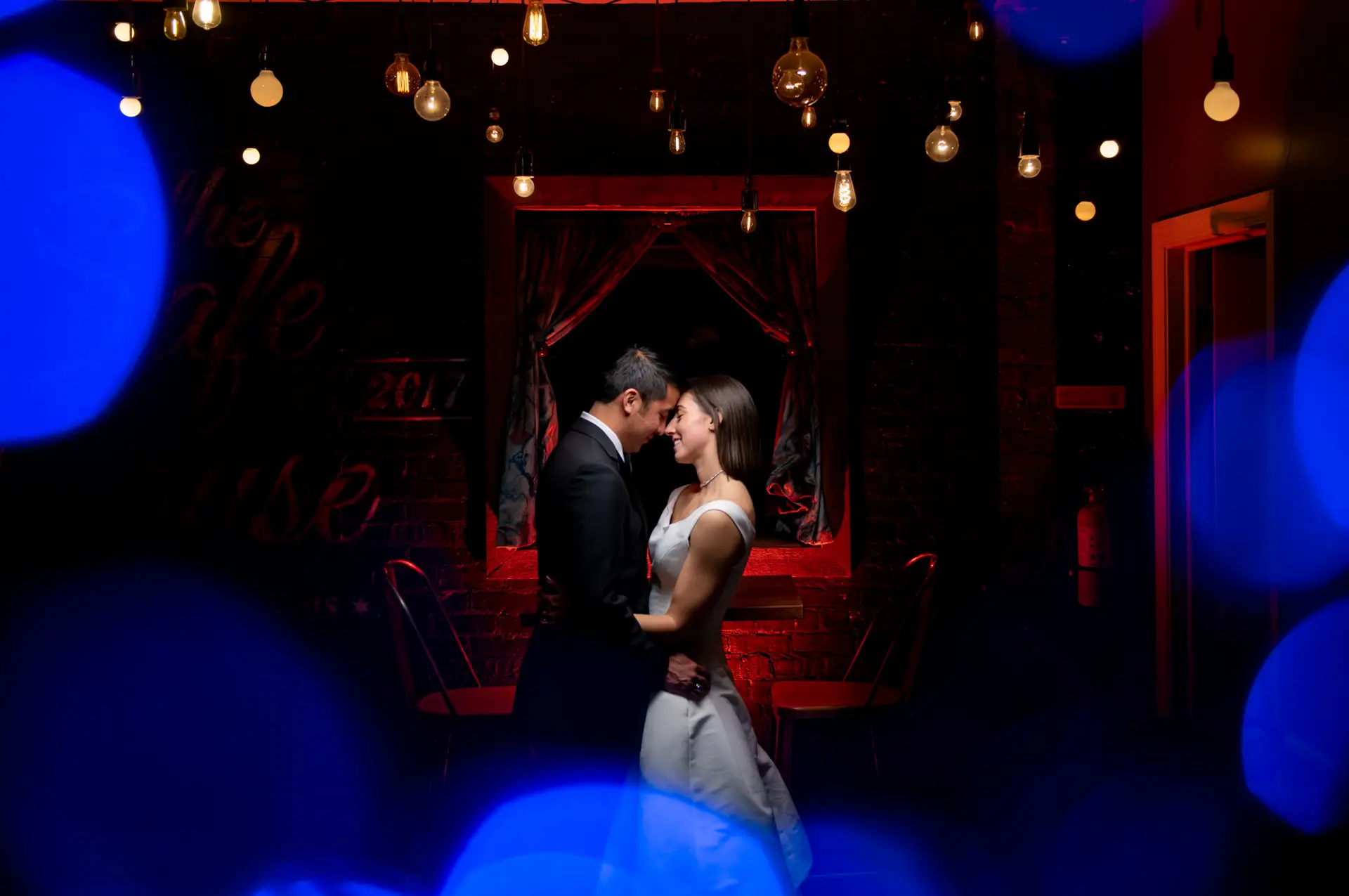 bride-groom-together-under-lights-with-red-background-the-joinery-chicago